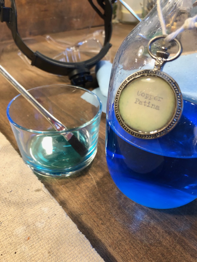 a bottle of blue liquid labeled Copper Patina, and a small jar with a brush and some liquid in it